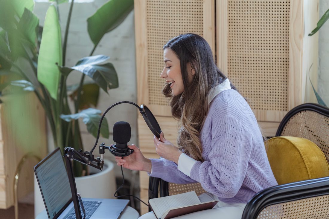 A woman recording a podcast with a laptop and microphone at home.