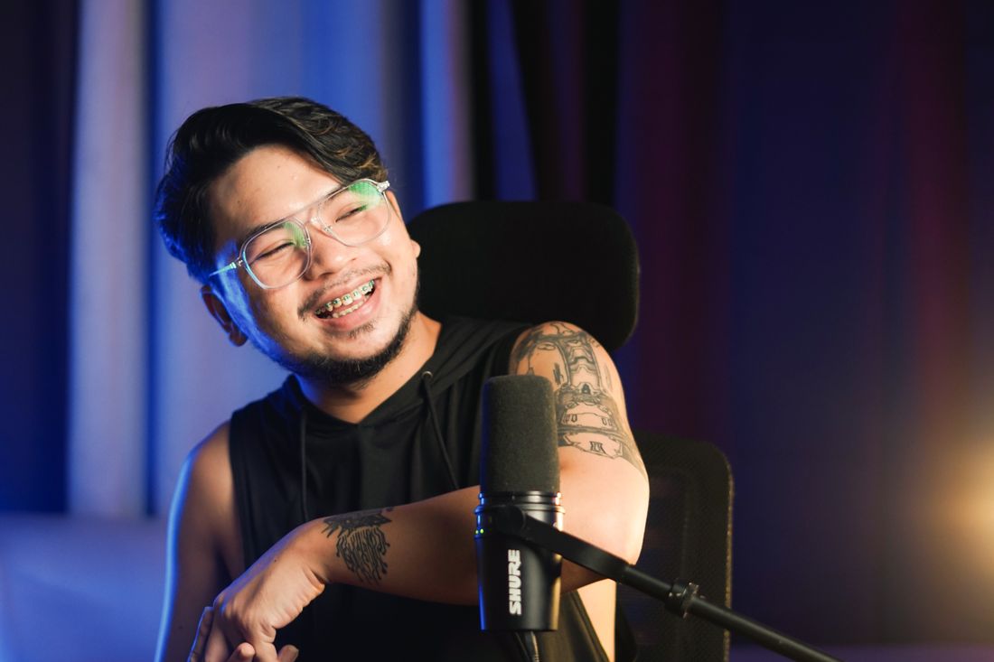 A smiling content creator sitting at a microphone.